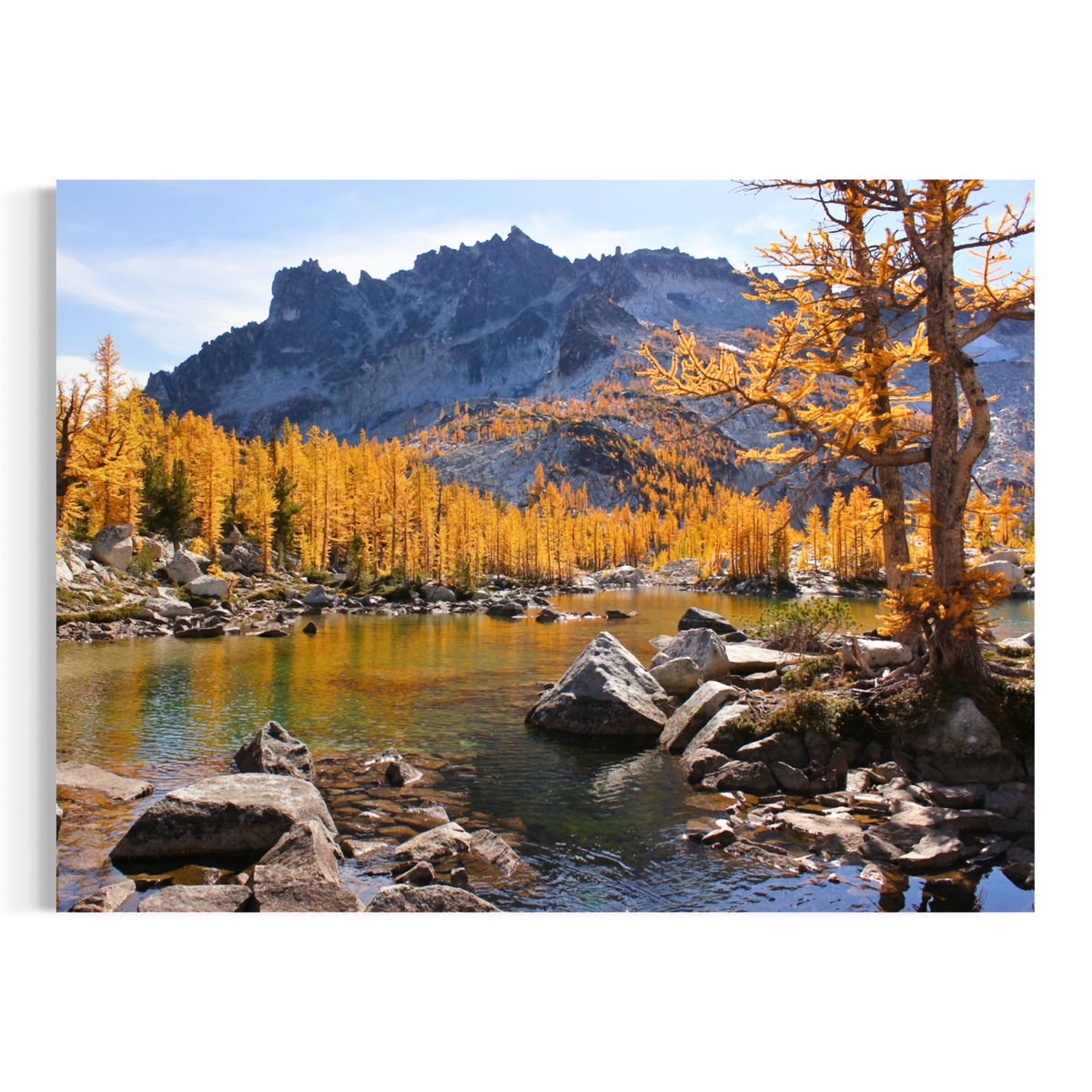 A rectangular wall art print showing a mountain landscape with a rocky river, golden autumn trees, and blue sky, displayed against a plain white background.