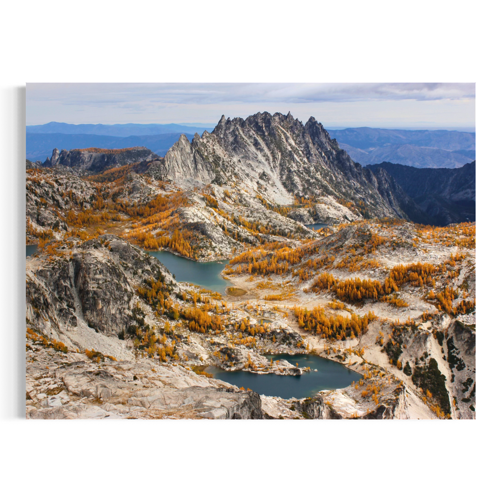 A rectangular wall art print showing a mountain landscape with rocky peaks, blue lakes, and golden autumn trees, displayed against a plain white background.