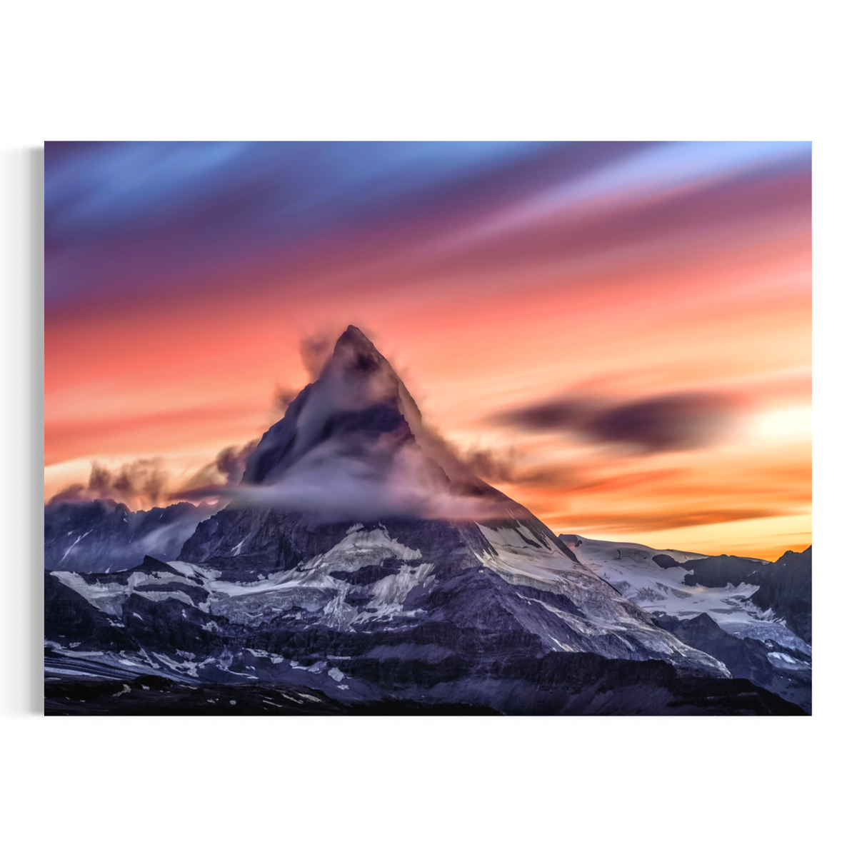 A rectangular wall art print or canvas showing a dramatic mountain peak at sunset, with pink, orange, purple, and blue sky streaks and snow-covered slopes below, displayed against a light gray background.