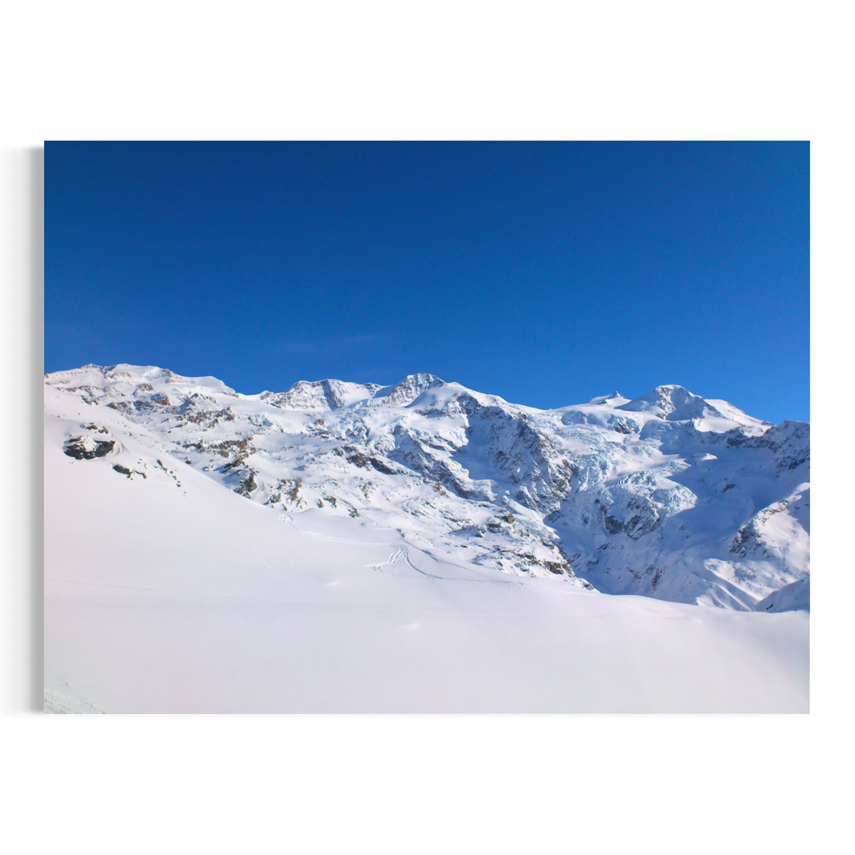 A horizontal canvas wall art print depicting a snowy mountain landscape under a clear blue sky, shown as a mockup on a white background.