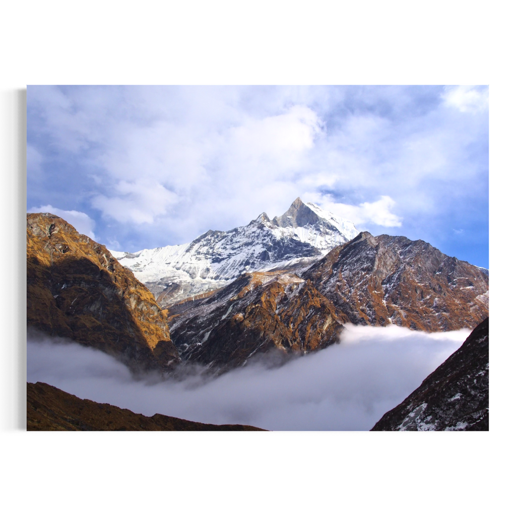 A rectangular wall art print or canvas showing a mountain landscape with a snow-capped peak, rocky brown slopes, clouds, and blue sky, displayed against a plain white background.