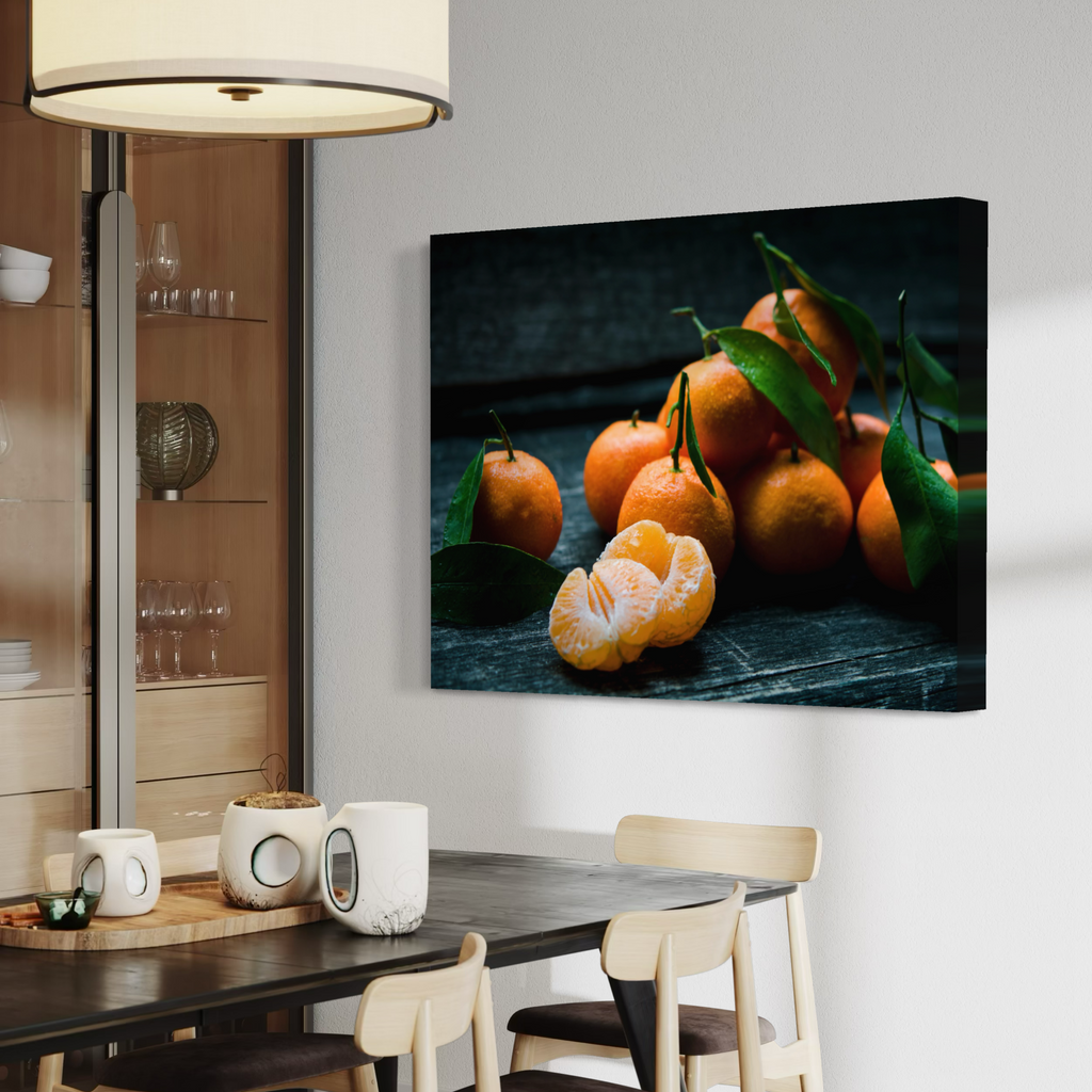A wall art canvas print showing a cluster of bright orange mandarins with green leaves on a dark rustic surface, displayed on a white wall above a dining table in a modern interior setting.