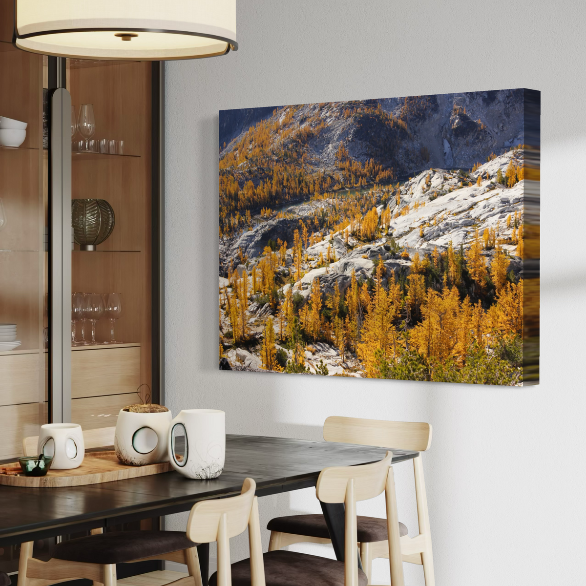 A canvas wall art print depicting a mountain landscape with golden yellow larchwood trees and snow, displayed on a light gray wall in a modern dining room setting.