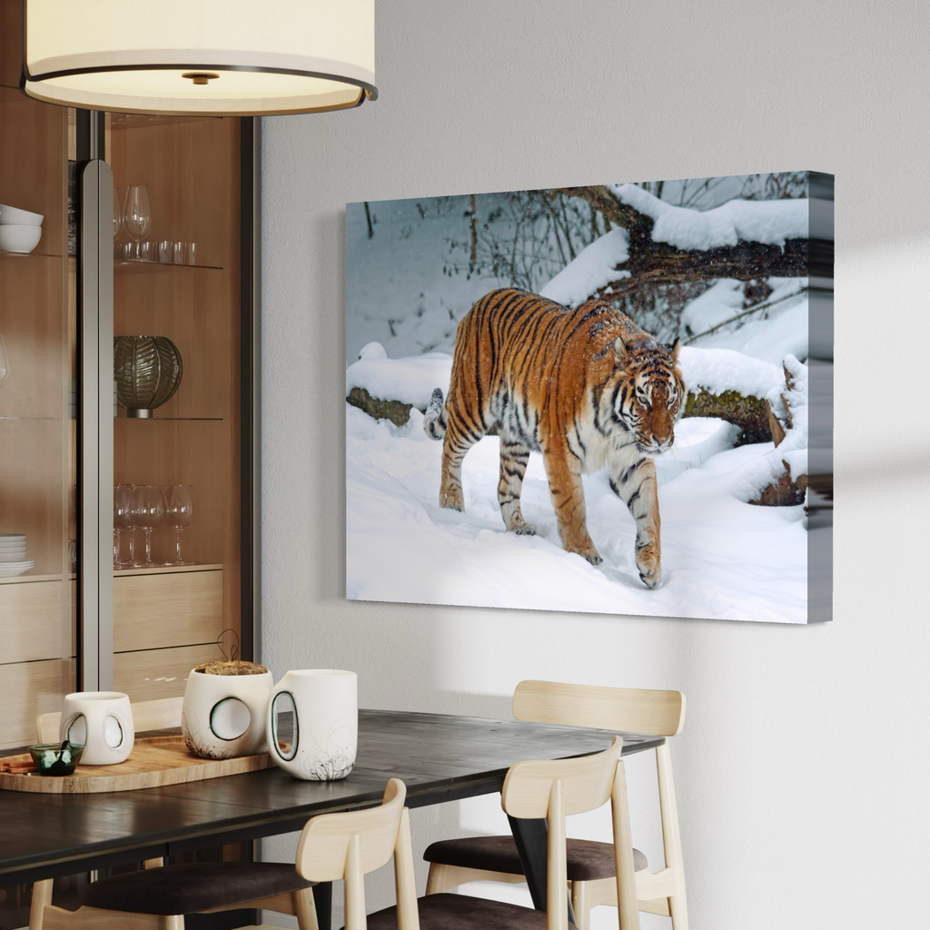 A canvas wall art print depicting a tiger walking through deep snow, displayed on a light gray wall in a modern dining room setting with a dark wood table and chairs.