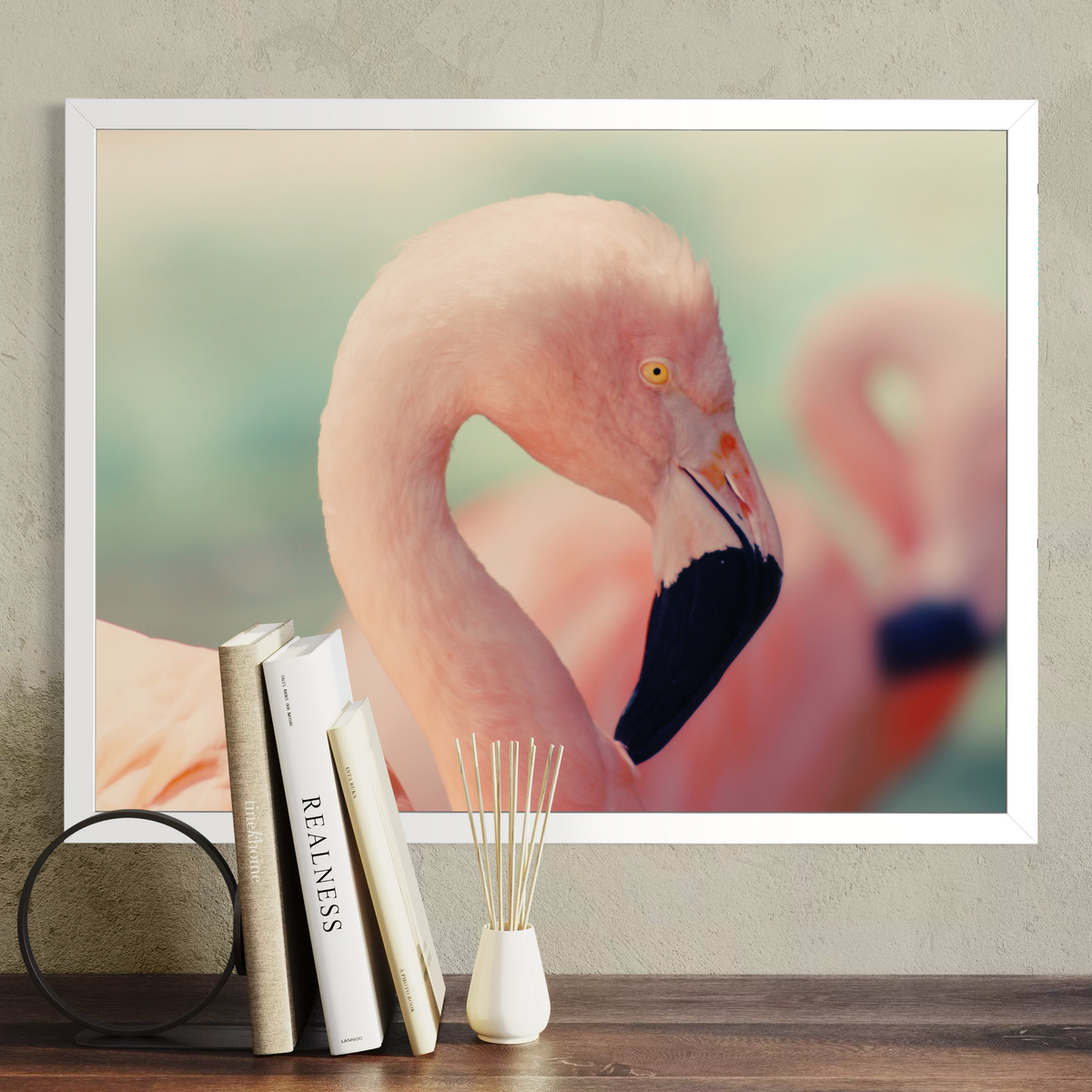A framed art print of a pink flamingo hanging on a textured gray wall above a wooden table with books and a small vase.