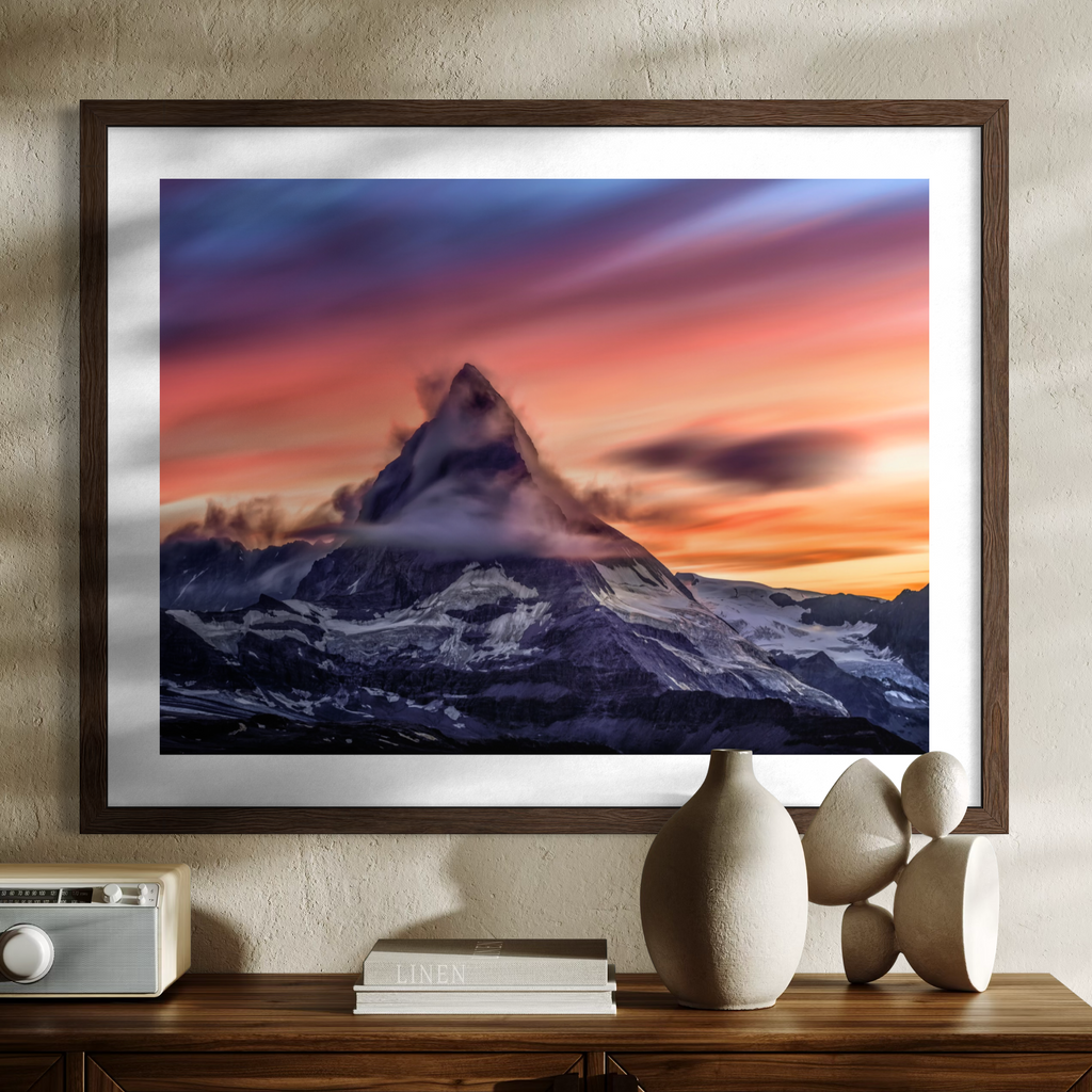 A framed art print of the Matterhorn mountain peak at sunset, displayed on a textured beige wall above a wooden console table with decorative ceramic vases and a radio.