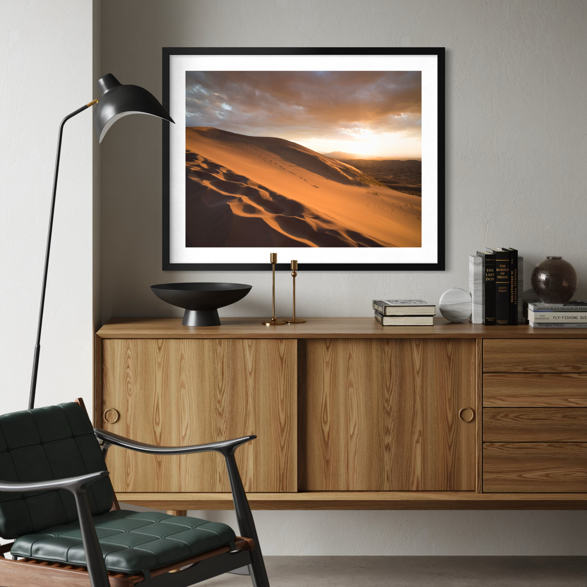 A framed art print depicting golden desert sand dunes under a dramatic sunset sky, styled on a wooden console table in a modern living room setting.