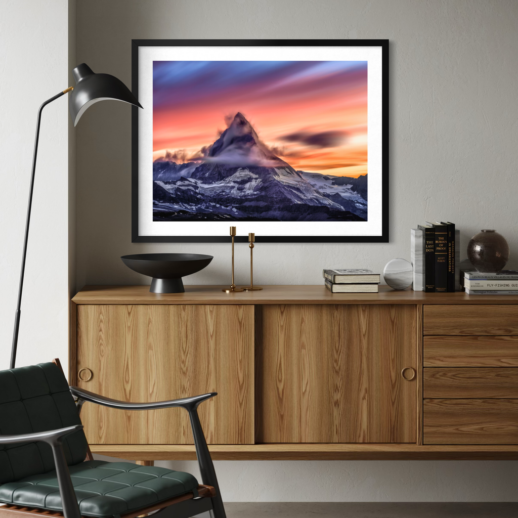 A framed art print of a mountain sunset hangs on a gray wall above a wooden credenza in a modern living room setting.