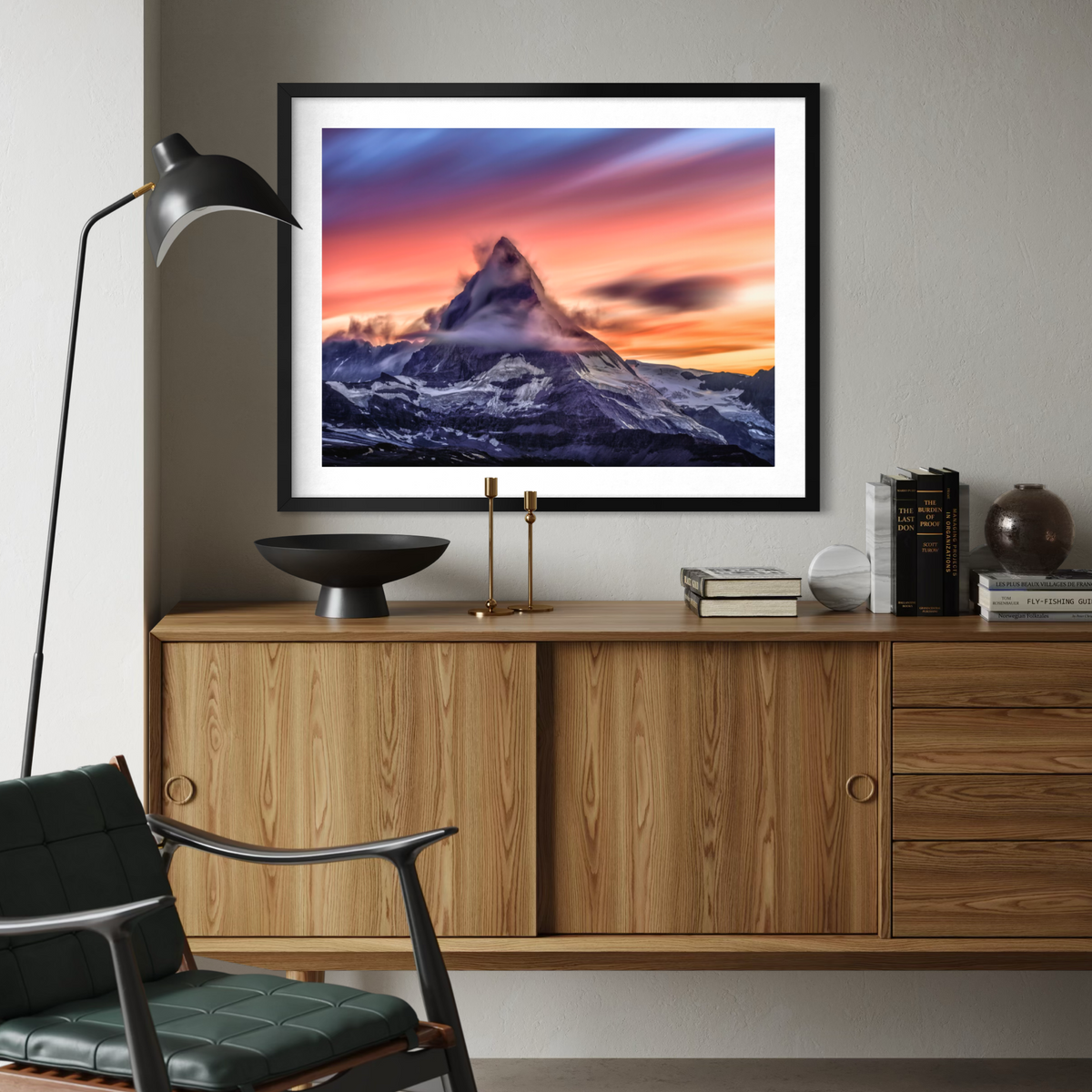 A framed art print of a mountain sunset hangs on a gray wall above a wooden credenza in a modern living room setting.