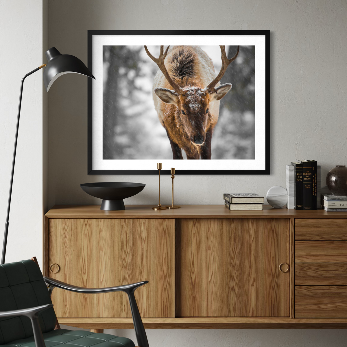A framed wall art print showing a close-up photograph of a stag with large antlers, displayed above a wooden cabinet in a modern living room setting.