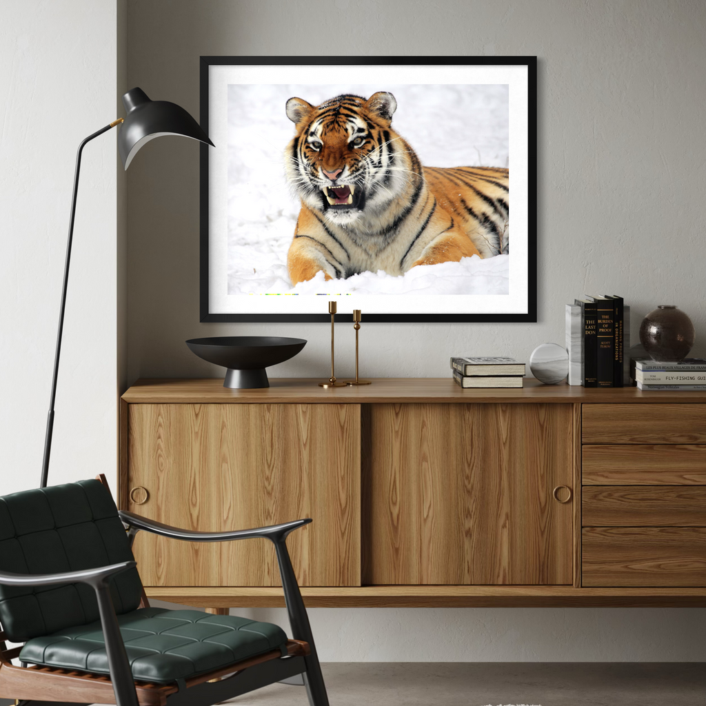 A black framed art print of a tiger in the snow hanging on a gray wall above a wooden credenza in a modern living room setting.