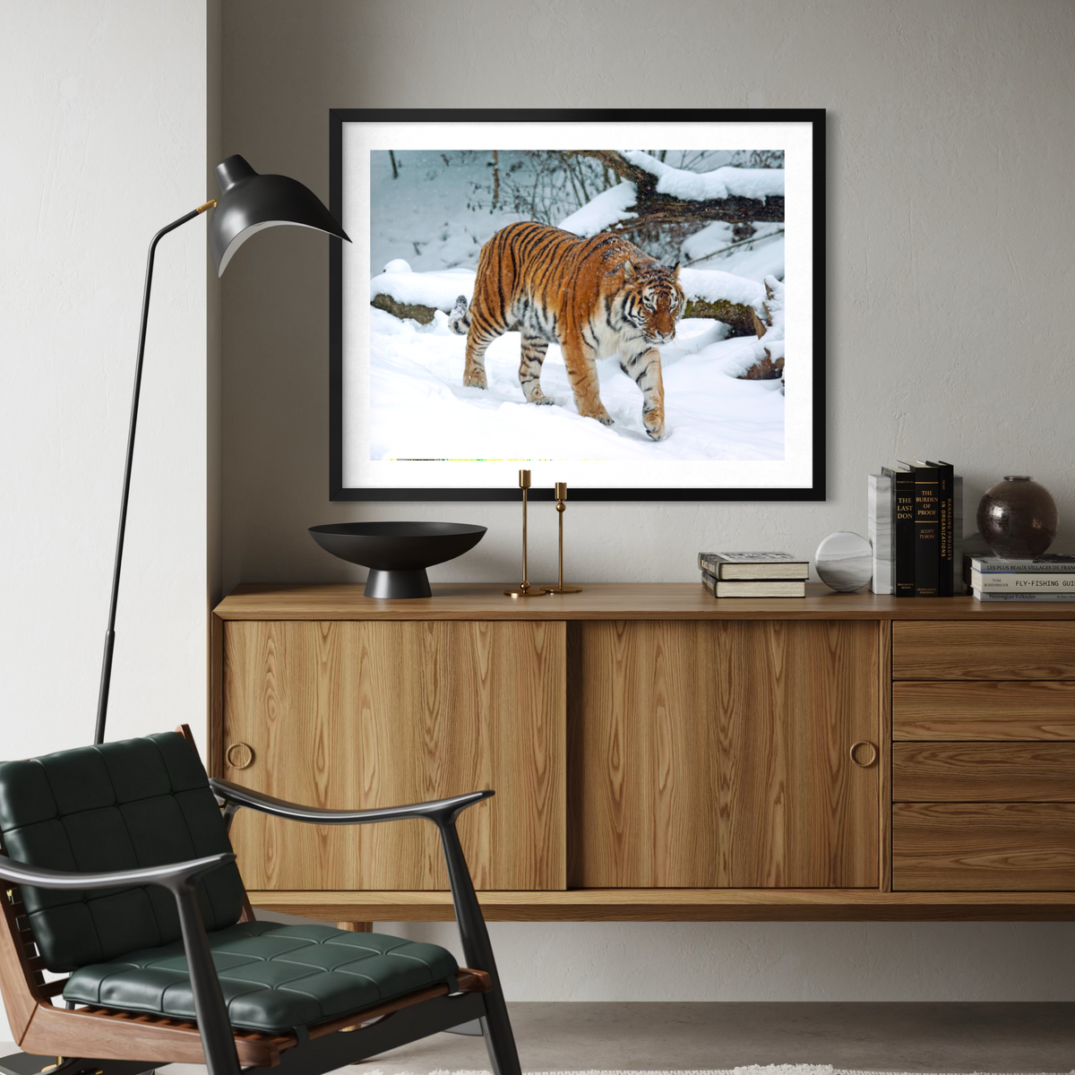 A framed art print of a tiger walking through a snowy forest, displayed on a wooden credenza in a modern living room setting.