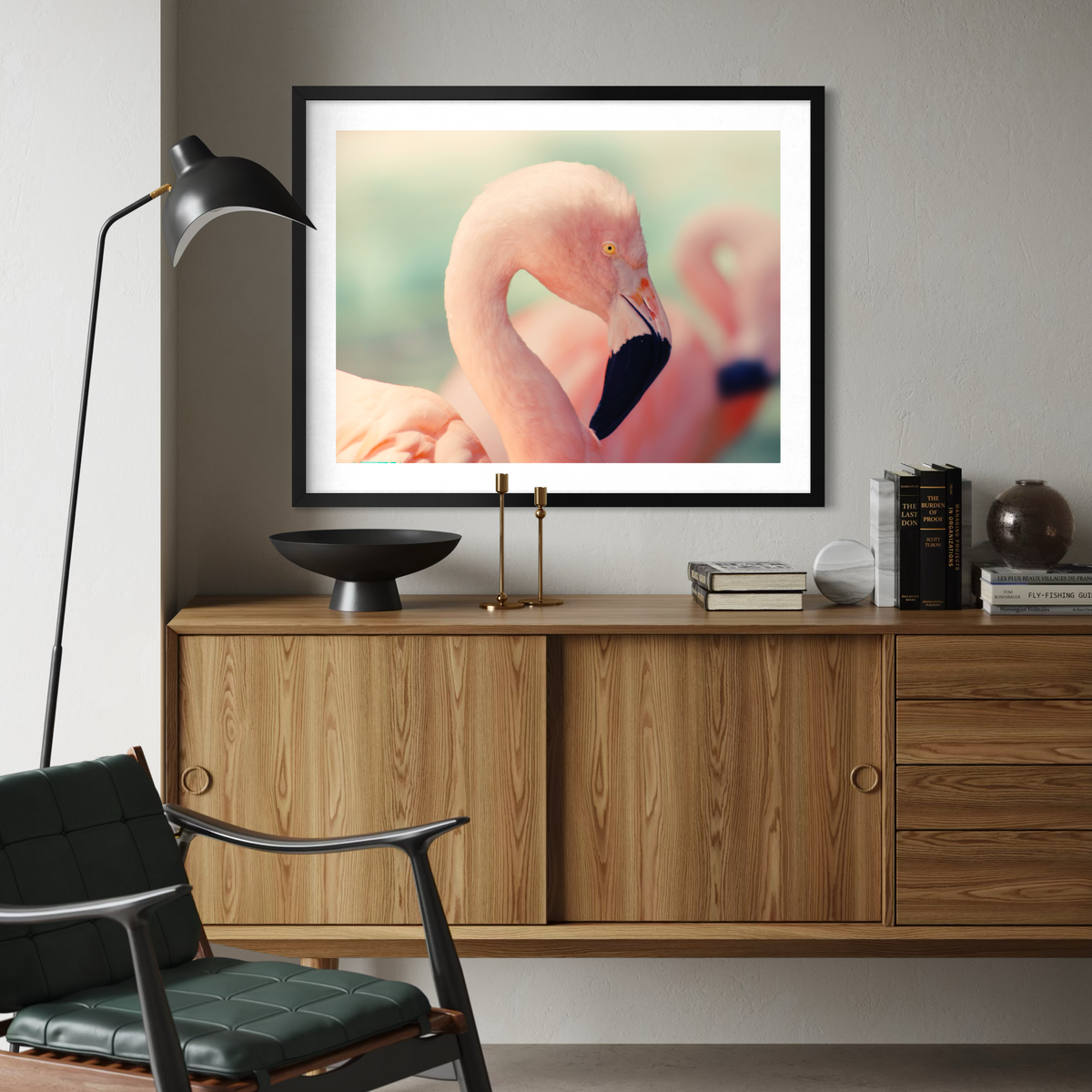 A black framed wall art print featuring a pink flamingo, displayed above a wooden credenza in a modern living room setting.